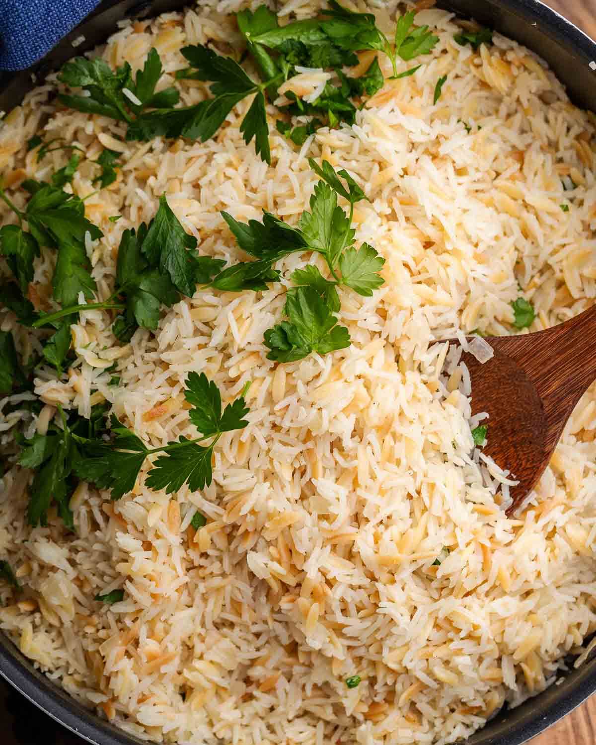 Rice pilaf in black pot with parlsey garnish and walnut spoon.