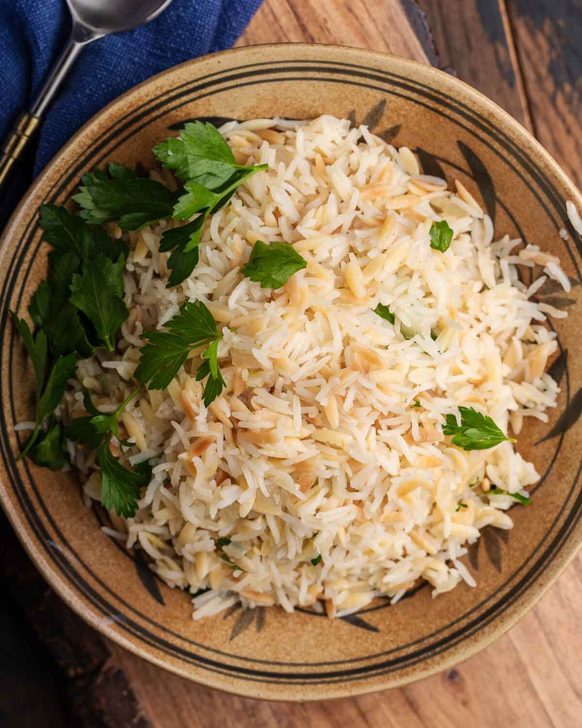 Rice pilaf in orange bowl on wooden board.