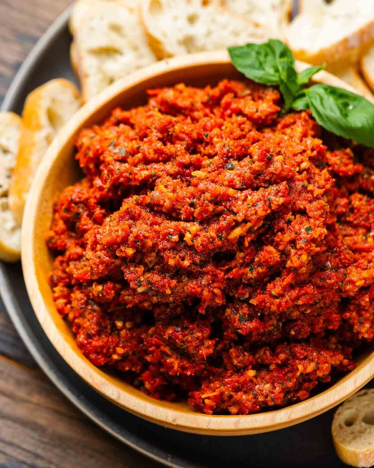 Sun dried tomato tapenade in wood bowl with pieces of bread.