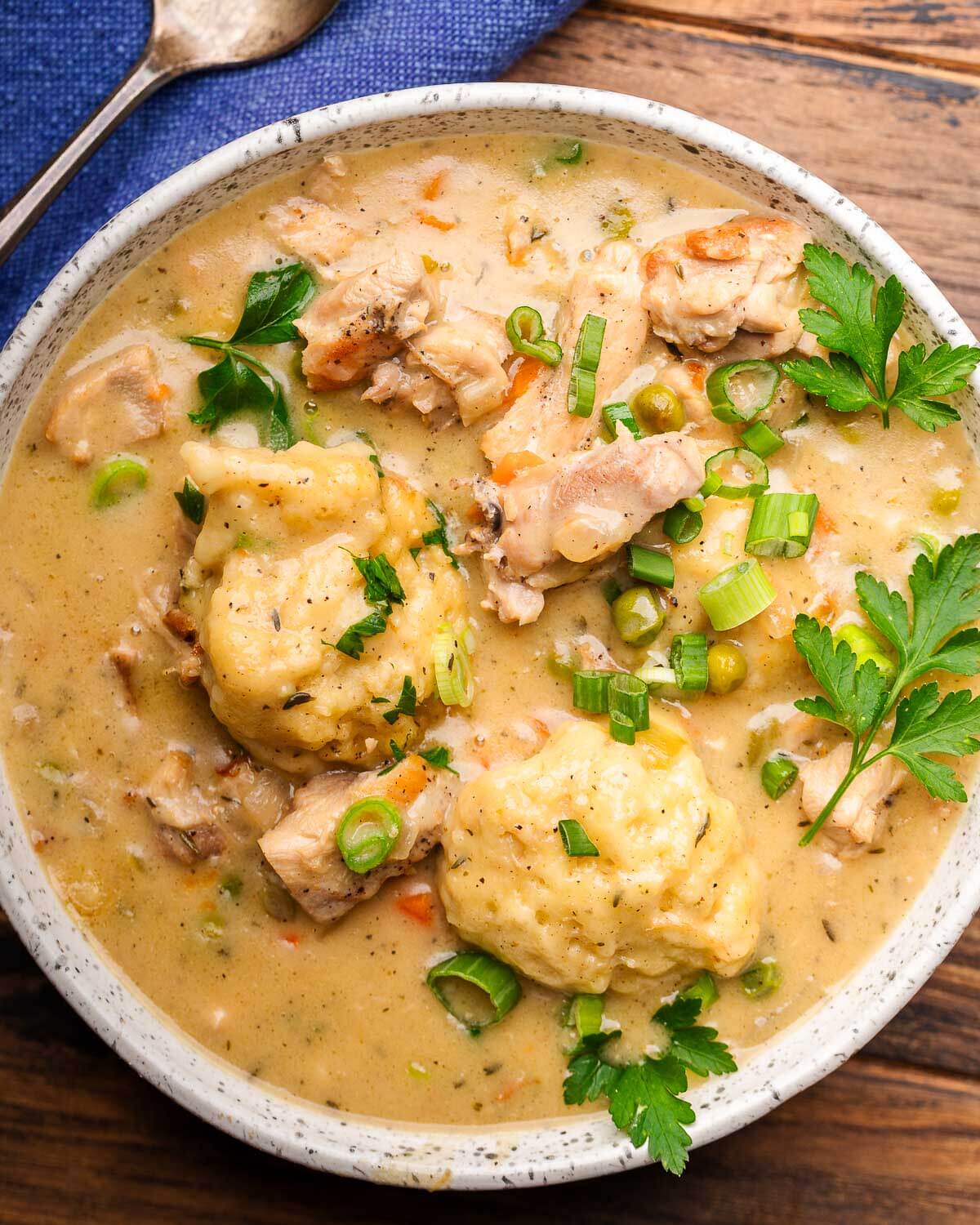 Chicken and dumplings in white bowl with blue napkin.