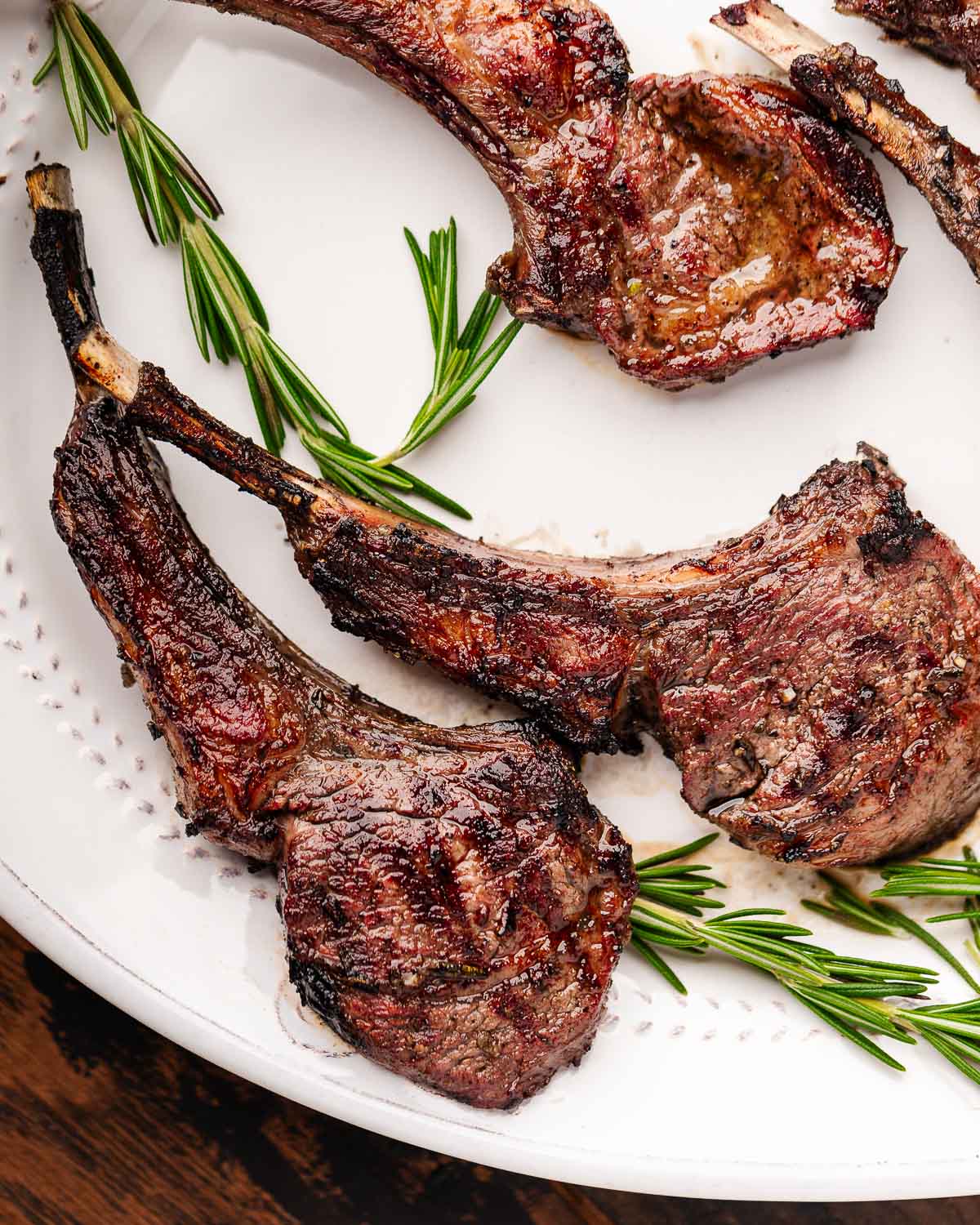 Grilled lamb chops on white plate with rosemary garnish.