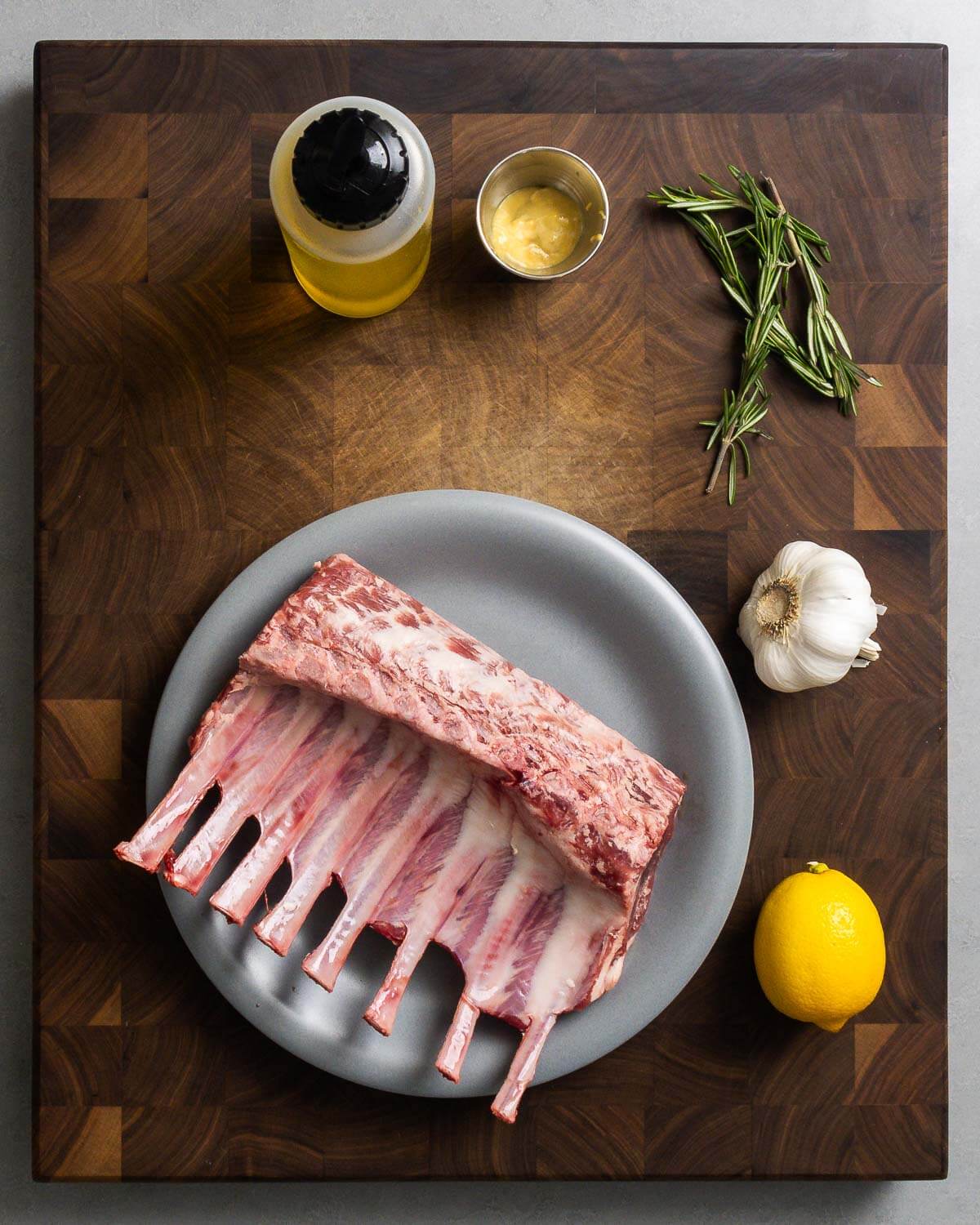 Ingredients shown: olive oil, Dijon mustard, rosemary, garlic, lemons, and rack of lamb.