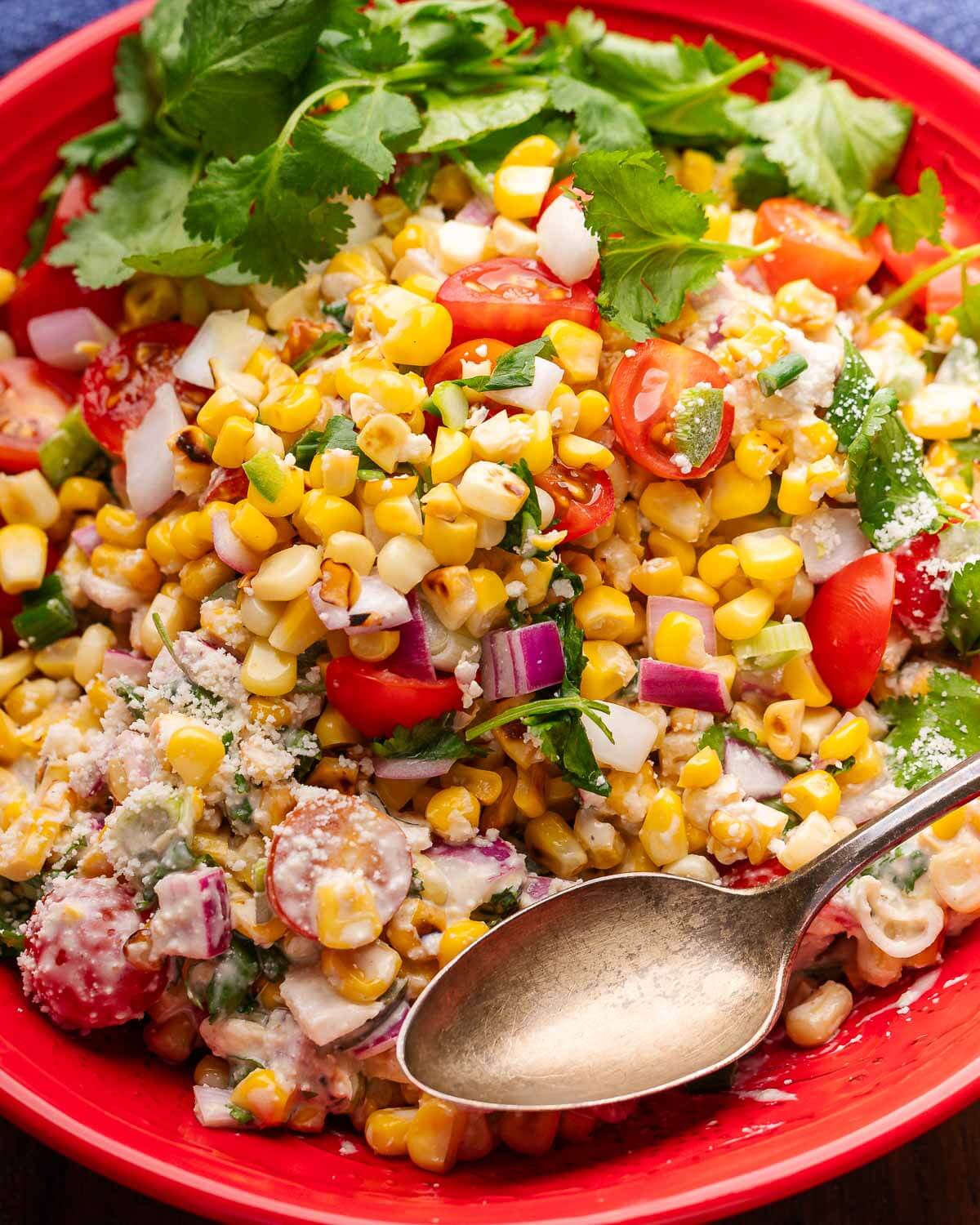 Mexican street corn salad in red bowl with spoon and cilantro garnish.