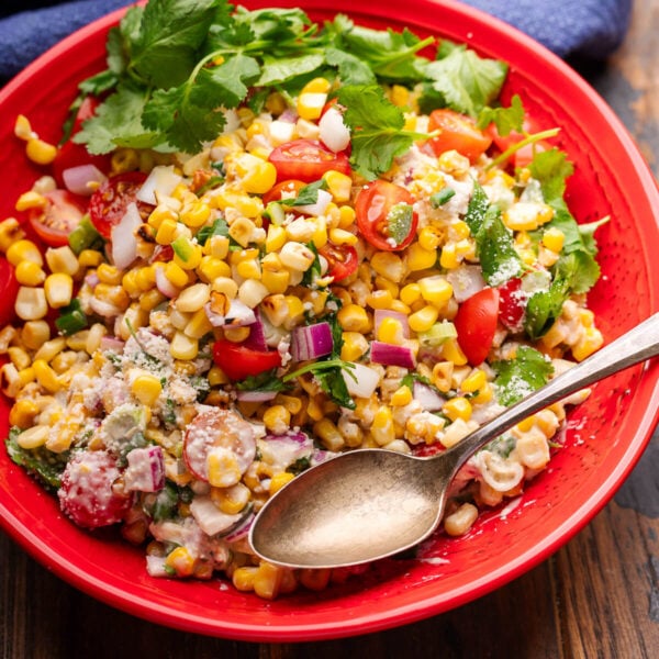 Mexican street corn salad in red bowl with cilantro garnish.