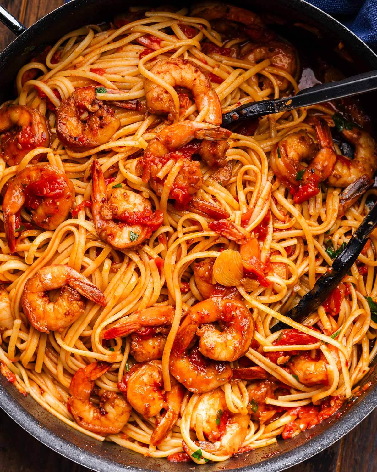 Close up photo of shrimp fra diavolo in black pan with tongs.