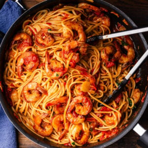 Shrimp fra diavolo in black pan with tongs.