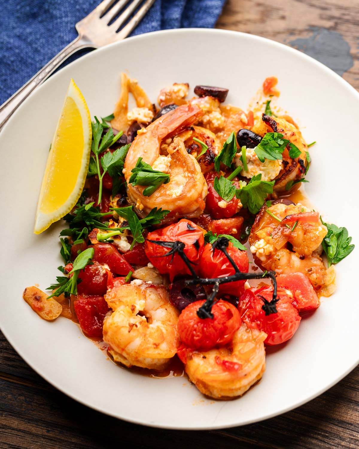 Shrimp saganki on white plate with lemon wedge and parsley garnish.