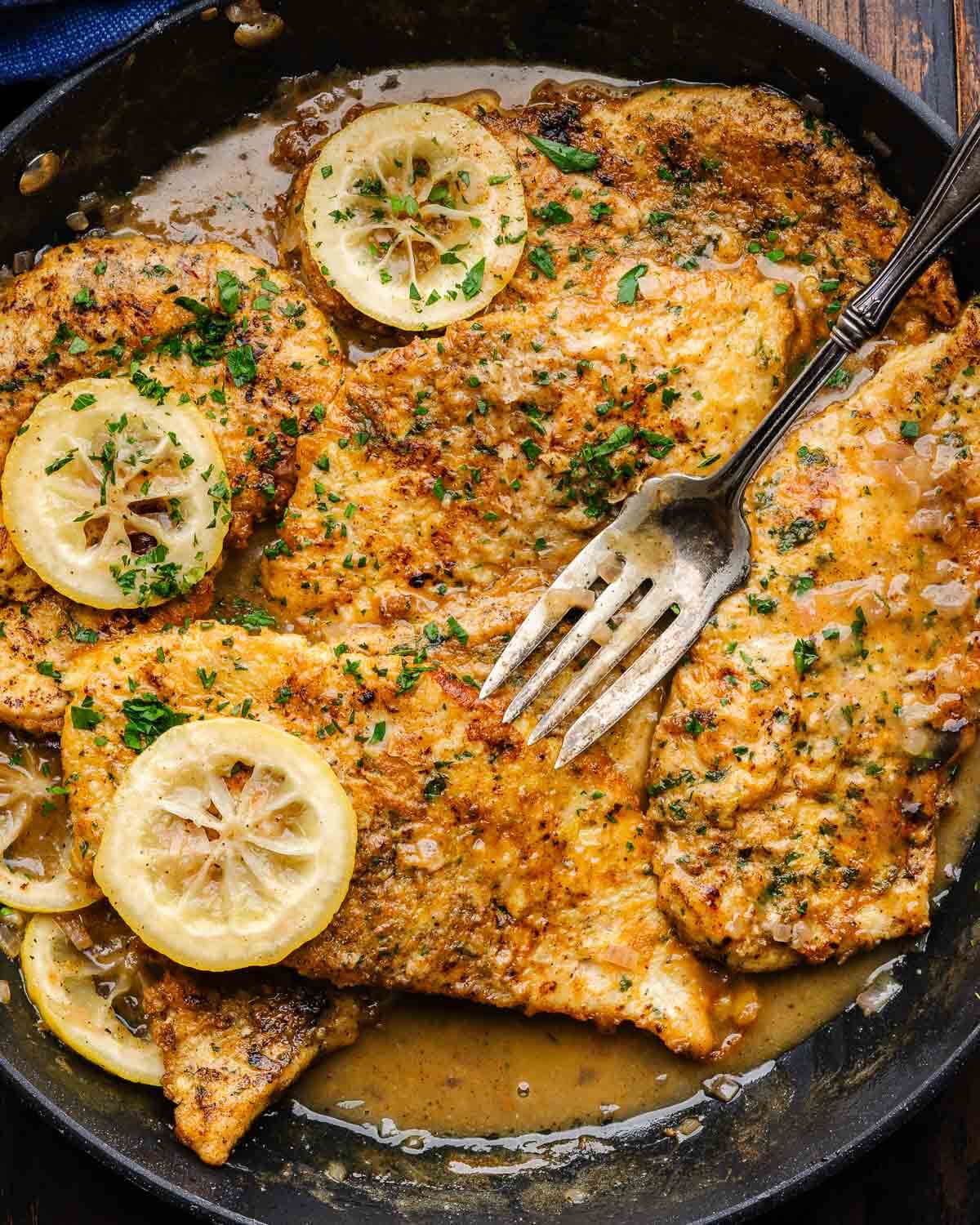 Chicken Francese in black pan with lemon slices.