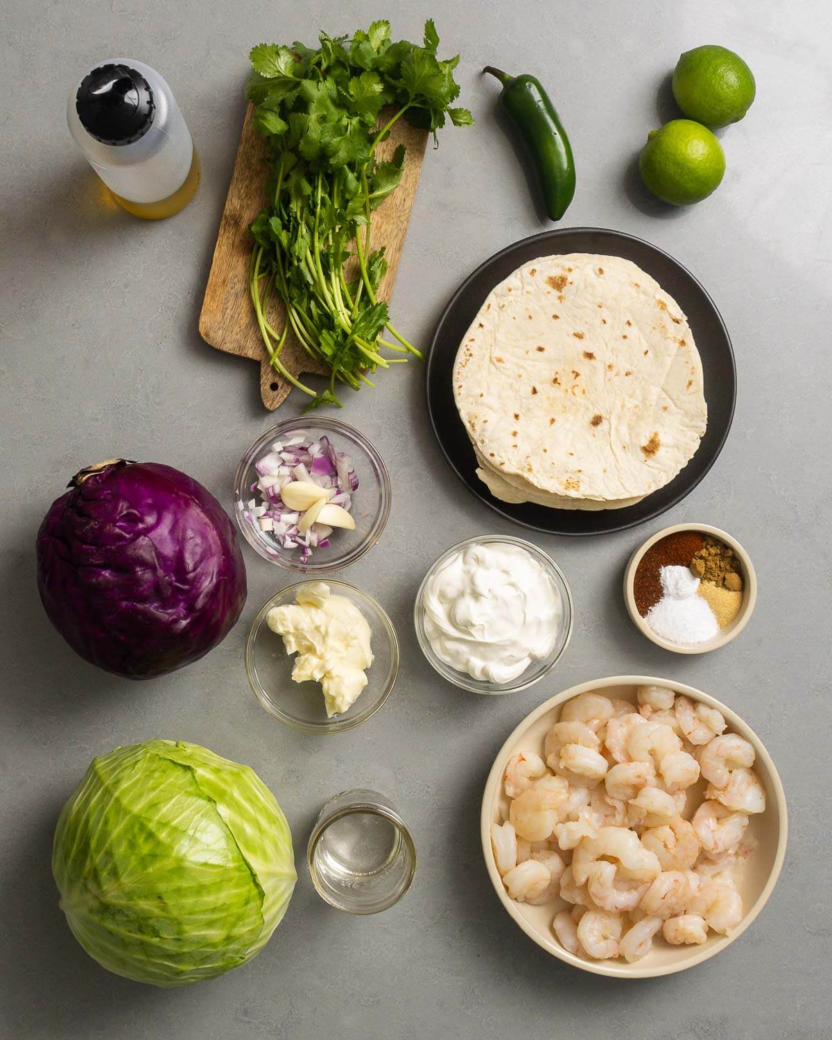 Ingredient shown: olive oil, cilantro, jalapeno, limes, tortillas, garlic, onion, cabbage, mayonnaise, sour cream, spice and chili powder, tequila, and shrimp.