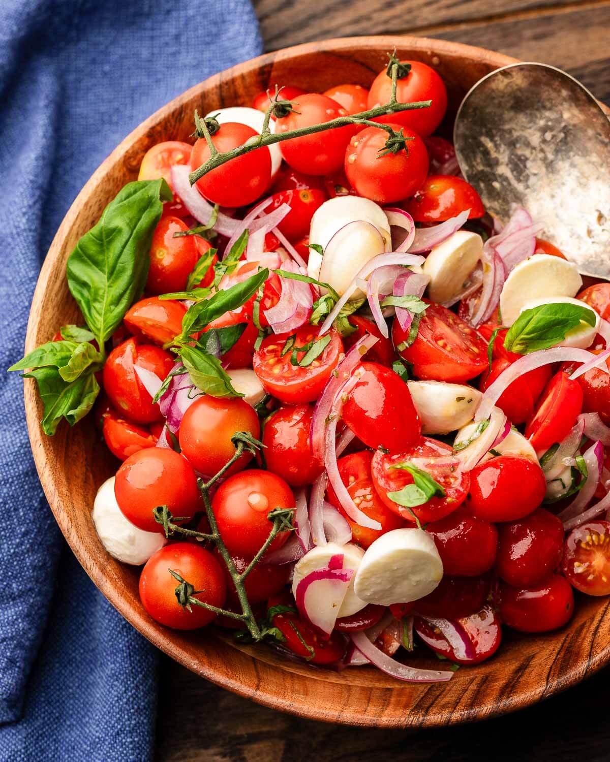Tomato mozzarella salad in wood bowl with blue napkin.
