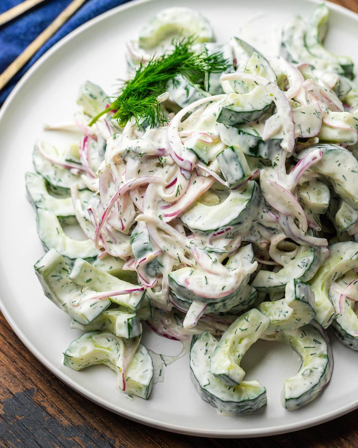 Creamy cucumber salad on white plate with dill garnish.