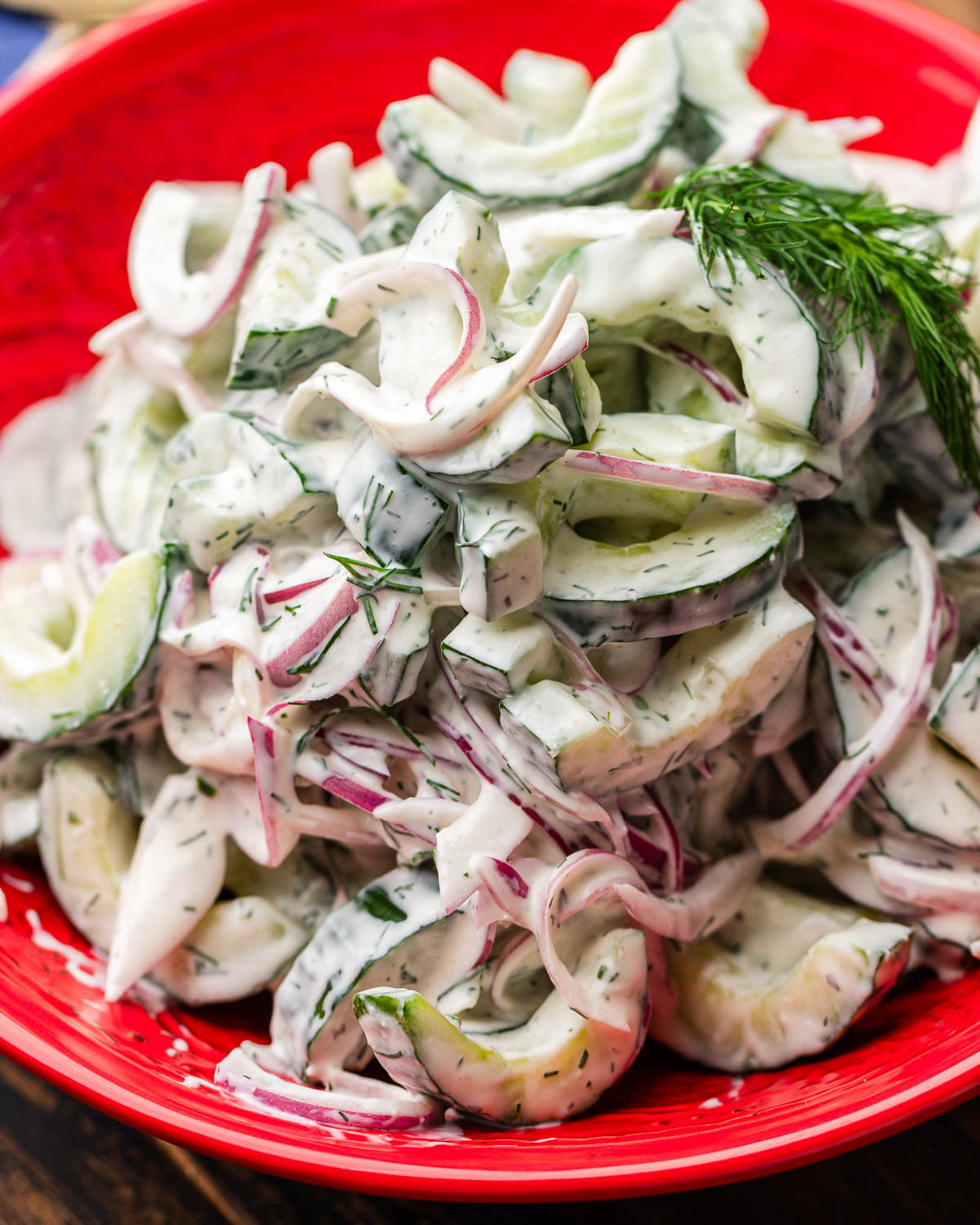 Creamy cucumber salad in red bowl with dill garnish.