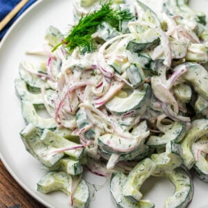 Creamy cucumber salad on white plate with dill garnish.