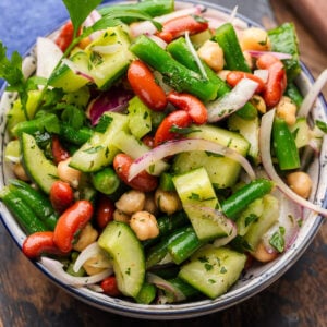Mixed bean salad in white and blue bowl topped with parsley and red onions.