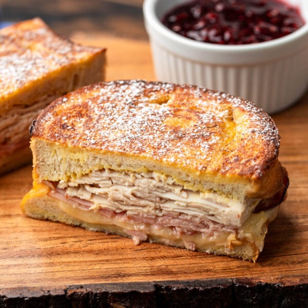 Monte Cristo sandwich along with bowl of raspberry jam on wooden board.