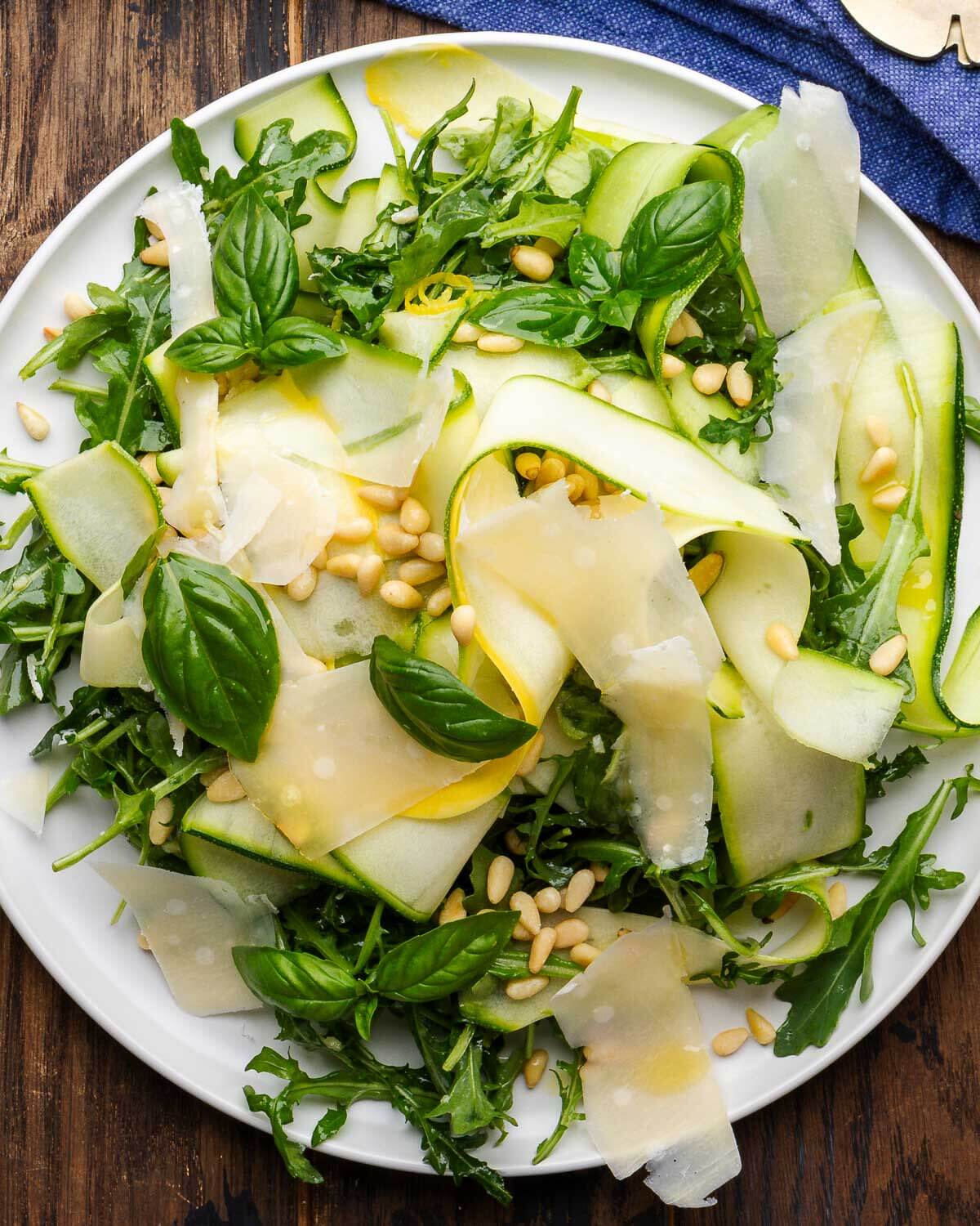 Shaved zucchini salad on white plate with blue napkin in the background.