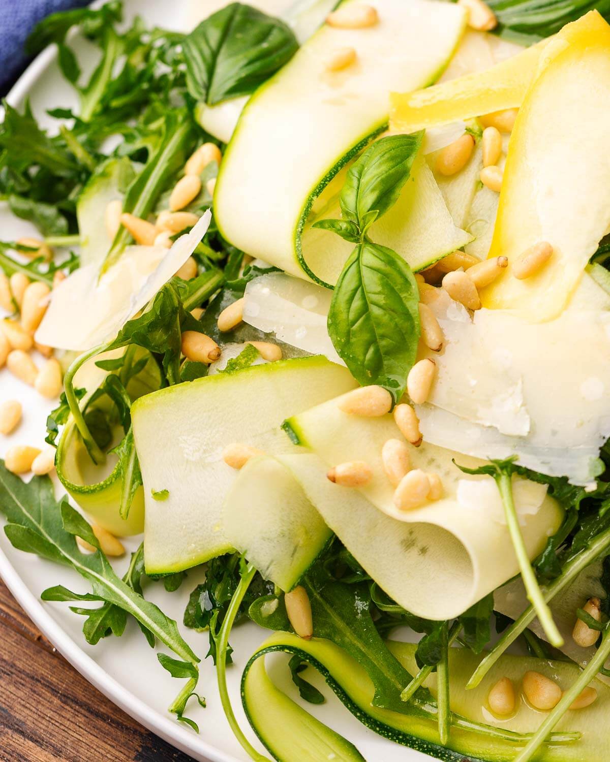 Closeup shot of ribbons of shaved zucchini, basil, and pine nuts salad on white platter.