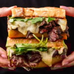 Two halves of a steak sandwich held in hands.