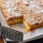 New York crumb cake with slice cut out of it on baking sheet.