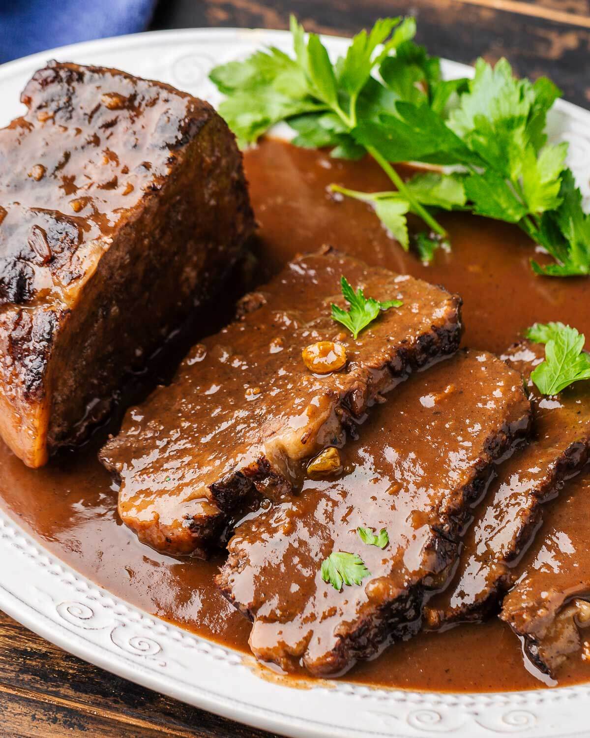 Platter with sliced sauerbraten covered in gravy.