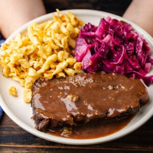 Sauerbraten with spaetzle and red cabbage on plate.