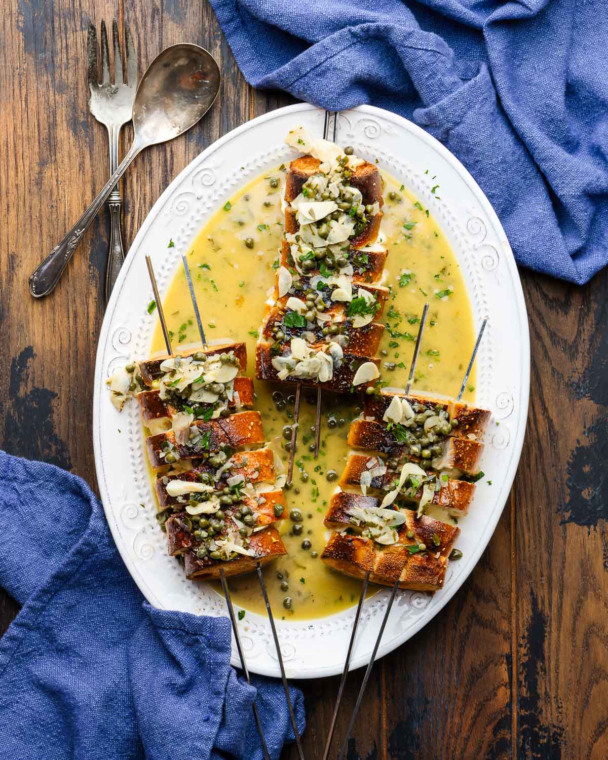 Overhead shot of large white platter with three Spiedini alla Romana with caper sauce poured on top.