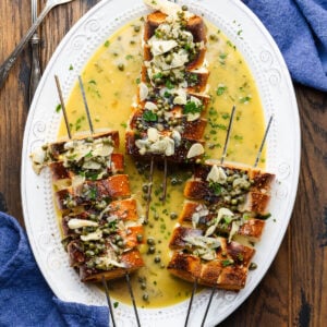 Three spiedini alla Romana with caper sauce poured on top and in the platter.