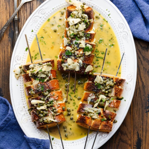 Three spiedini alla Romana with caper sauce poured on top and in the platter.