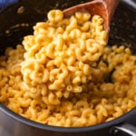 Large ladle spooning elbow mac and cheese over pot.