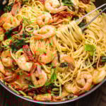 Creamy sun dried tomato shrimp pasta in black pan with tongs.