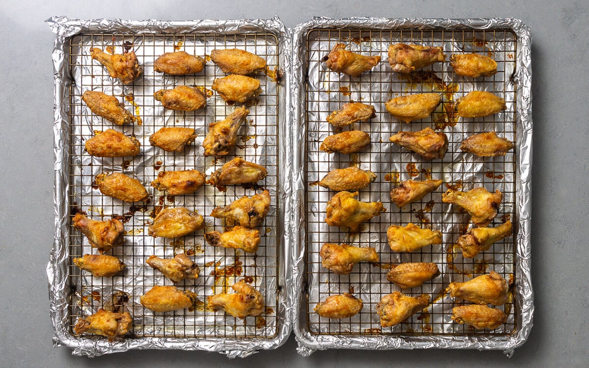 Two foil covered baking sheets with chicken wings.