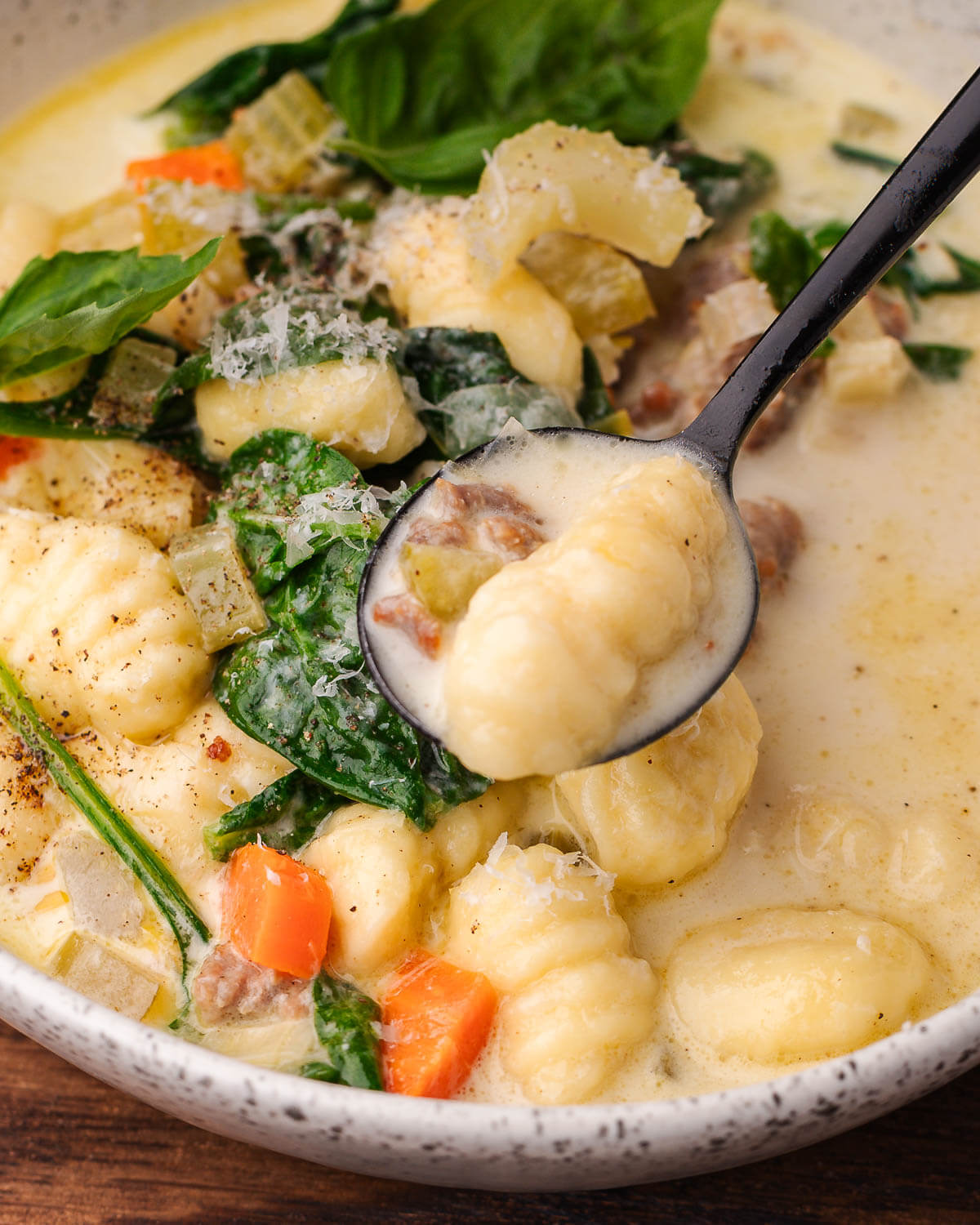 Black spoon holding gnocchi over soup bowl.