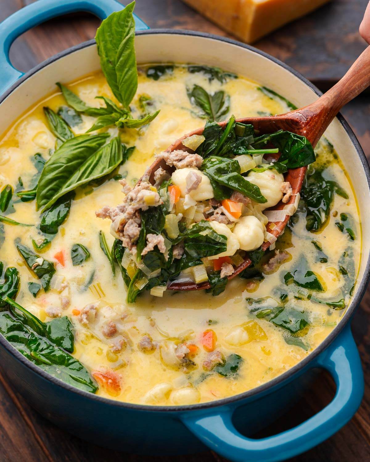 Large wooden ladle holding big scoop of sausage gnocchi soup over Dutch oven pot.