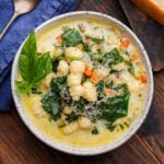 Sausage gnocchi soup in white bowl with basil garnish and grated cheese.