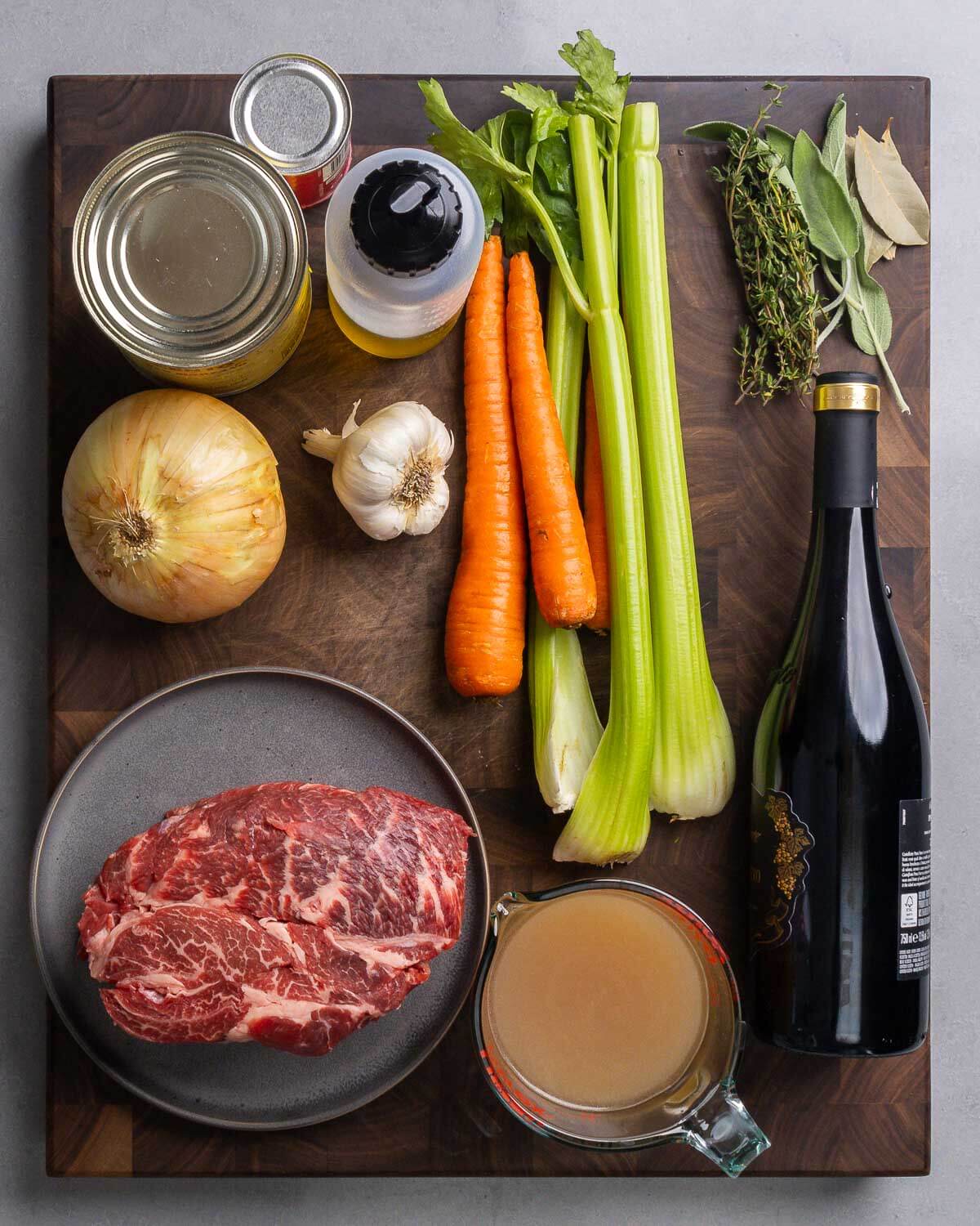 Ingredients shown: canned tomatoes, olive oil, carrots, celery, herbs, onion, garlic, chuck roast, beef stock, and bottle of red wine.