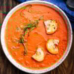 White bowl with creamy tomato soup topped with croutons and chiffonade of basil.