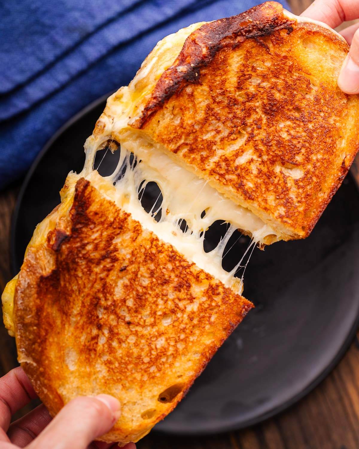Hands pulling apart grilled cheese over black plate.