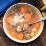 White bowl with Italian beef soup and block of Pecorino Romano in the background.
