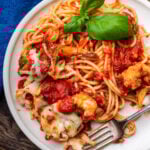 White plate with shrimp parmigiana, spaghetti, and basil garnish.