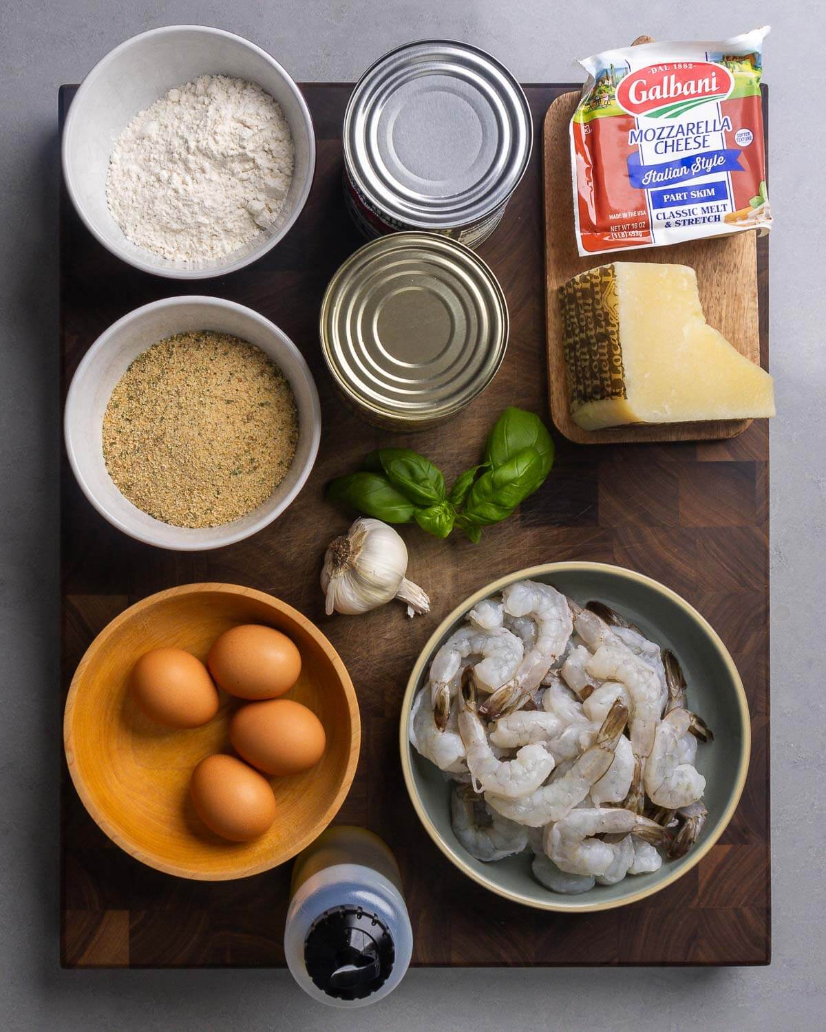 Ingredients shown: flour, canned tomatoes, mozzarella, Pecorino Romano, seasoned breadcrumbs, basil, garlic, eggs, shrimp, and olive oil.