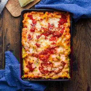 Baked ziti in black baking dish with blue napkins.