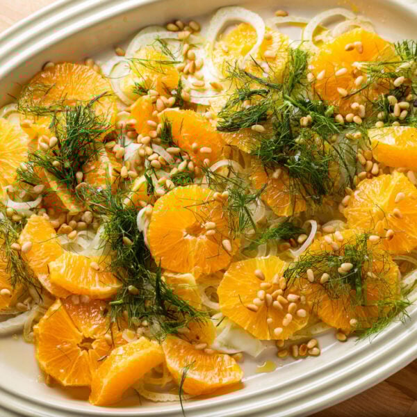 Platter with orange fennel salad topped with fennel fronds and pine nuts.