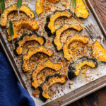 Parmesan roasted acorn squash on baking sheet with fork and blue napkin.
