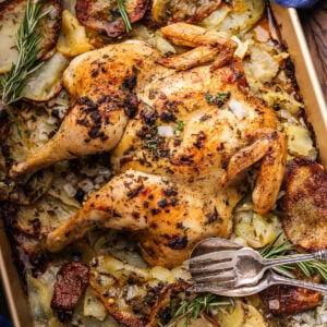 Spatchcock chicken and potatoes on baking sheet with fork and spoon.