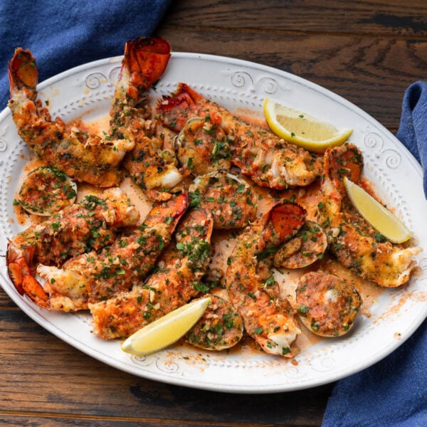 Lobster tails oreganata along with a few clams on white platter.