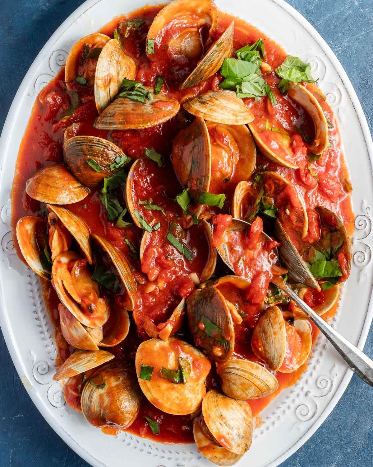 Clams in red sauce on white platter.