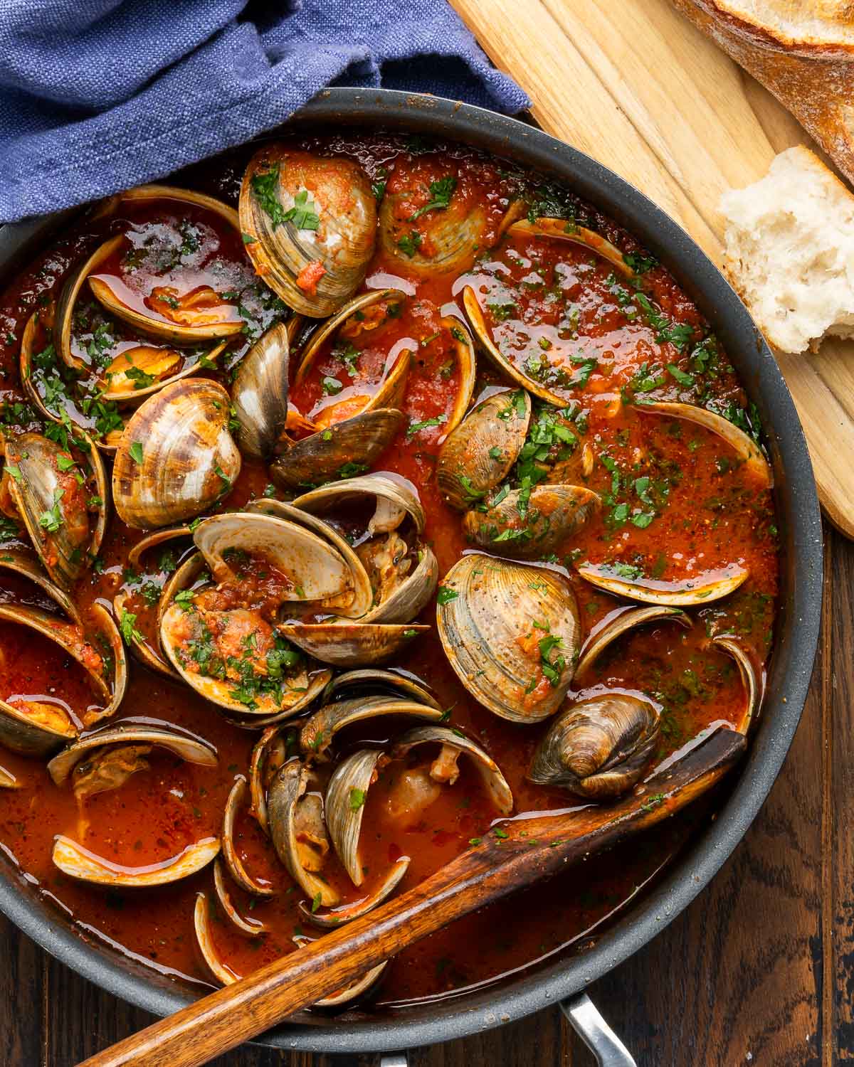Clams in red sauce in large pan with crusty bread on the side.