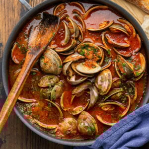 Clams in spicy tomato sauce in black pan.
