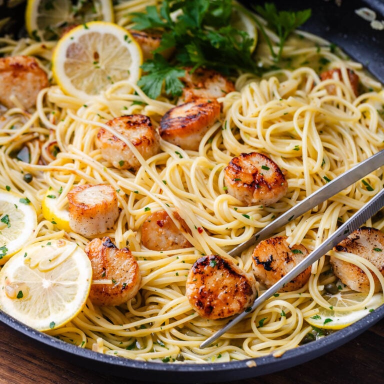 Lemon garlic scallop pasta in black pan with pasta tweezers.