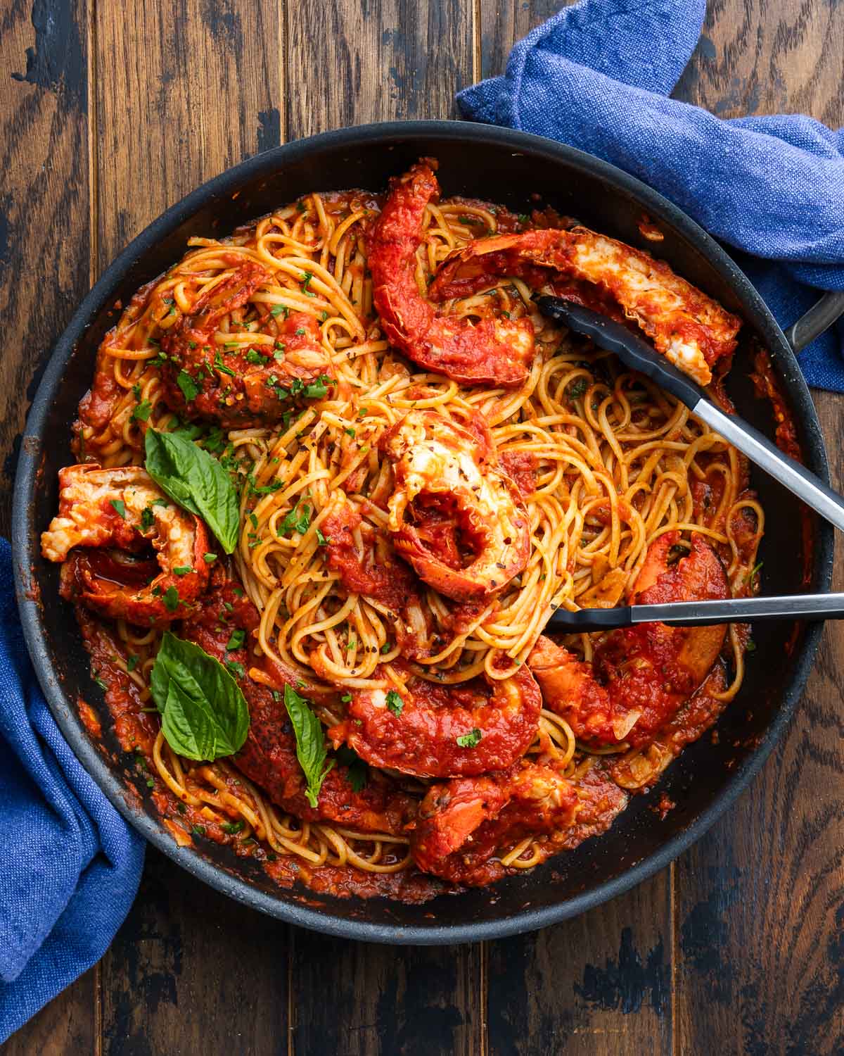 Lobster fra diavolo in black pan with basil garnish and 2 blue napkins.